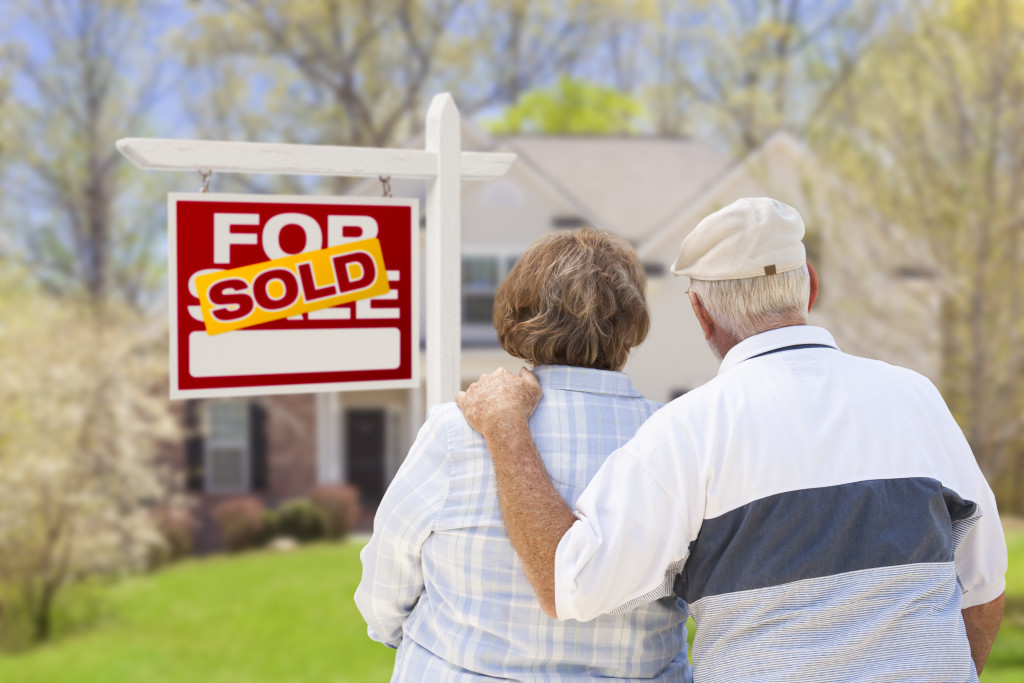 Happy Affectionate Senior Couple Hugging in Front of Sold Real Estate Sign and House